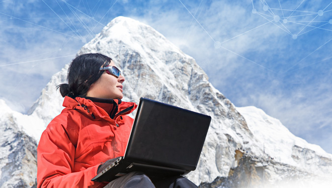 Woman seated with Laptop computer on lap seated at the base of a snow covered mountain.