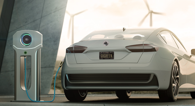 Image shows an electric car being charged next to a home. In the far distance are several wind turbines.
