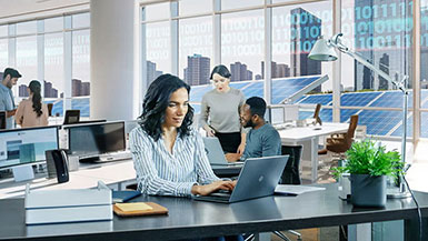 Diverse employees working in a modern office with solar panels outside and a cityscape in the background.