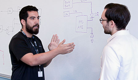 Electronics engineer talks with project manager as they choose a PCB.