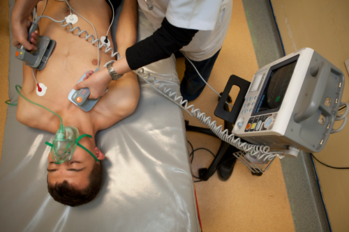 Figure 1. A hospital-style defibrillator with paddles. Note that there is an external electrocardiograph (ECG) or heart monitor on the patient, as evidenced by the white circles (electrodes) and leads (wires) on the chest.