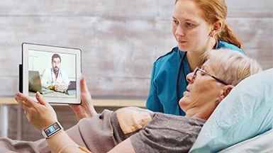 Elderly woman in home care video calls doctor, assisted by nurse in a calm, well-equipped room.