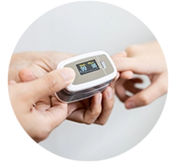Hand placing a fingertip pulse oximeter on another’s finger, displaying heart rate and oxygen levels.