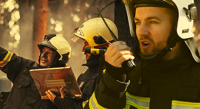 Firefighters in a forest wearing helmets and safety gear, coordinating efforts with a tablet and radio communication.