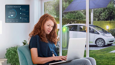 A girl in her living room with a wall-mounted energy monitor, overlooking an EV charging station and solar panels outside.