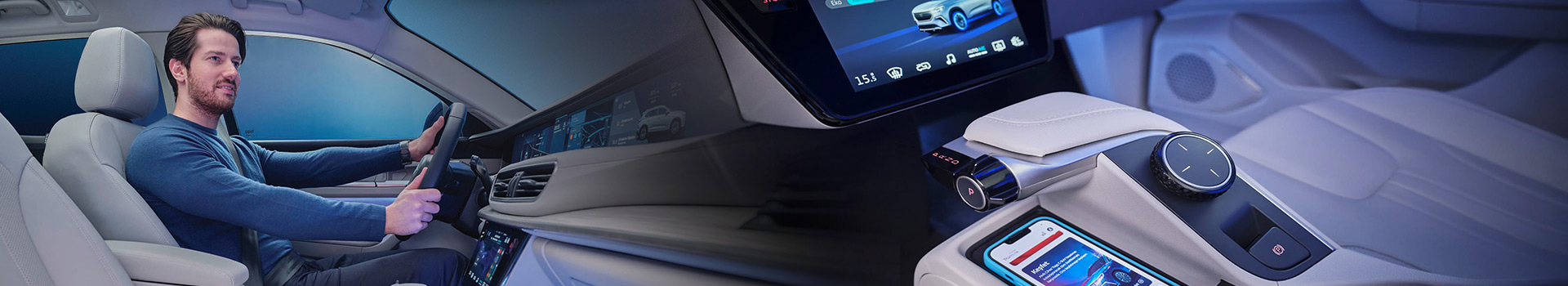 Man driving a modern car with an advanced digital dashboard, touchscreen controls, and a smartphone placed on a wireless charging pad, highlighting smart automotive technology.