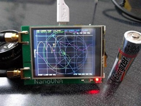 図 5. NanoVNA のオリジナル・ユニット。現在は中華製が多数販売。横の単三電池からその小ささが分かる。高橋 知宏 氏ご本人からご提供いただいた写真(高橋さん、写真をいただき、ありがとうございました!)